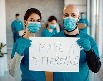 Volunteers with face masks working at charitable foundation and holding a placard with &apos;make a difference&apos; inscription while looking at camera.